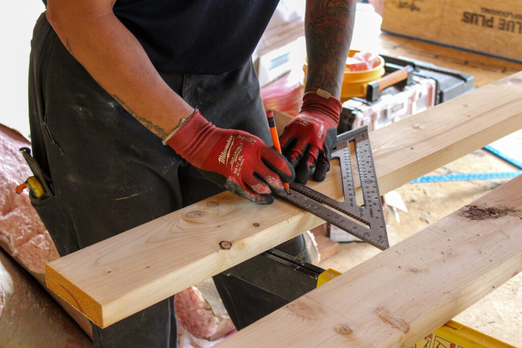 Professional carpenter measuring wood while framing a structure, showcasing commercial construction expertise through commercial design-build construction and integrated design build services with precision craftsmanship.