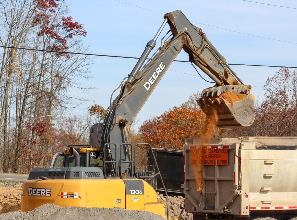 An excavator loading a dump truck on a commercial job site, illustrating commercial excavation services that prepare land for foundations, grading, and infrastructure development, including site grading & land preparation and utility & infrastructure excavation.