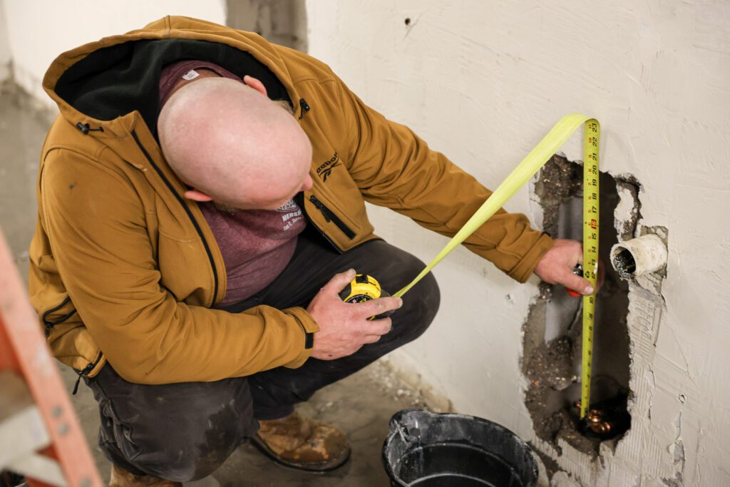 Professional Goodridge Construction plumber measuring a pipe during a commercial plumbing services installation to ensure accurate fitting and reliable system performance.