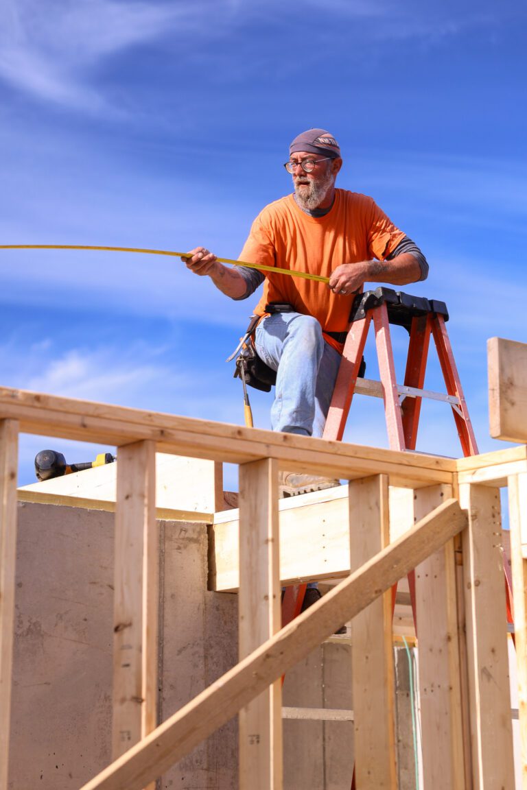 Goodridge Construction Group shows a professional carpenter on a ladder taking measurements while constructing a new home, highlighting expert craftsmanship.