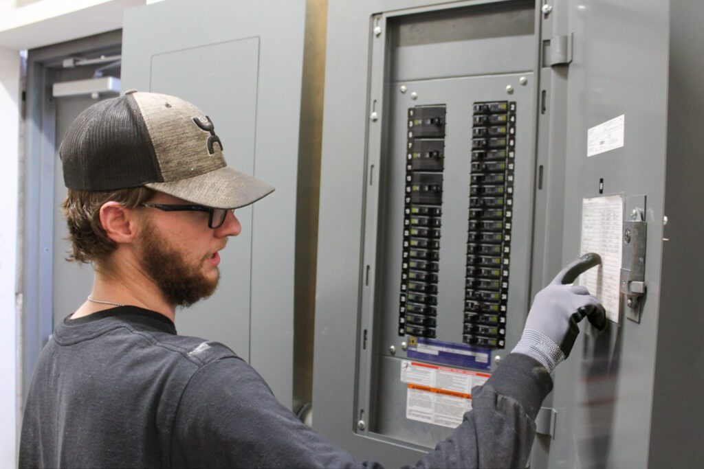Electrician inspecting a circuit breaker during an energy efficiency and conservation assessment, performing electrical panel upgrades and residential electrical system upgrades, including smart home electrical upgrades to improve home electrical performance.