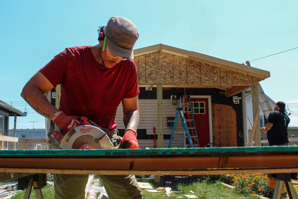 A carpenter cuts plywood while remodeling a house roof, showcasing expert exterior remodeling services, garage remodeling services, and deck and porch remodeling services.