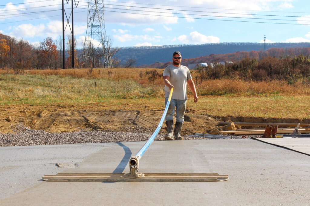 A professional concrete worker leveling cement on a driveway installation, demonstrating expert residential concrete services and foundation construction