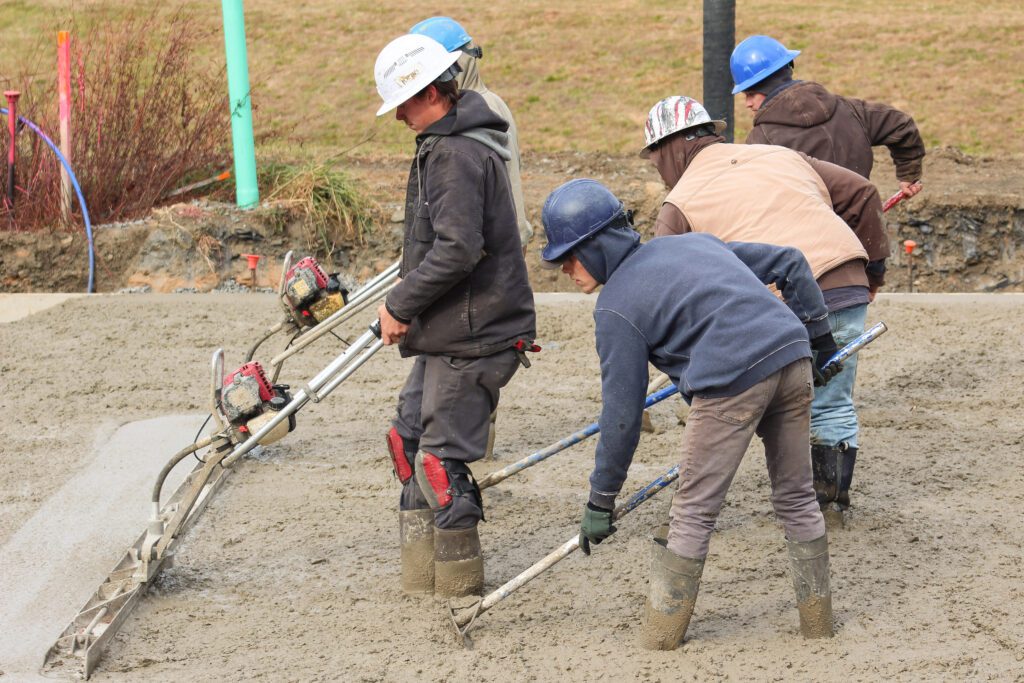 A crew of professional concrete workers smoothing freshly poured concrete on a commercial site, demonstrating commercial concrete services that ensure durable, level, and precise surfaces, including foundation & structural concrete and utility & infrastructure concrete.