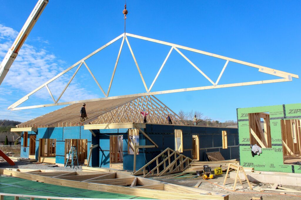 A crane lowers roof trusses on a framing project, highlighting expert craftsmanship in new construction services, home addition services, and garage construction services.