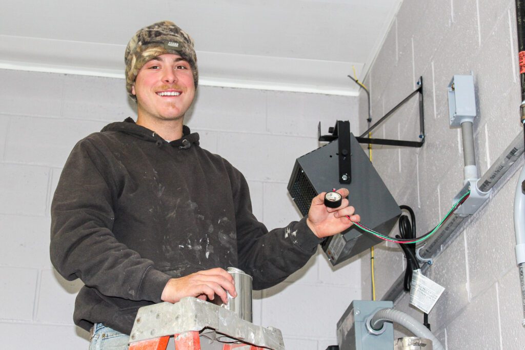 A professional electrician installing a sound speaker in a commercial building as part of a Commercial Electric System upgrade, ensuring proper wiring, safety, and integrated functionality.