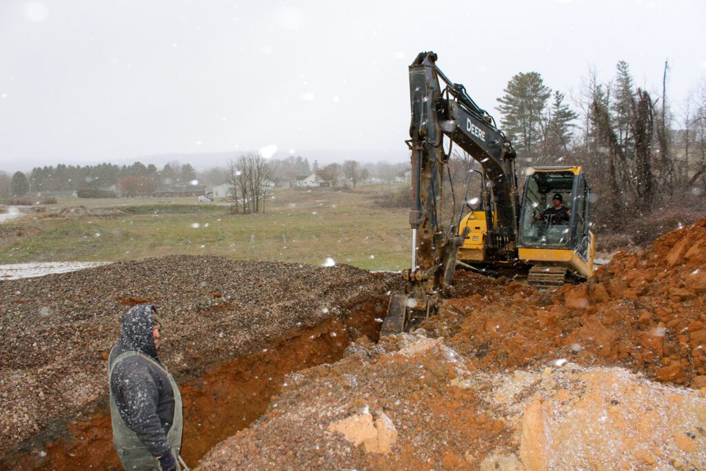 An excavator performing utility trenching on a commercial construction site, supporting drainage construction, commercial foundation preparation, and commercial site development services by creating stable footers and utility pathways for long-term structural performance.